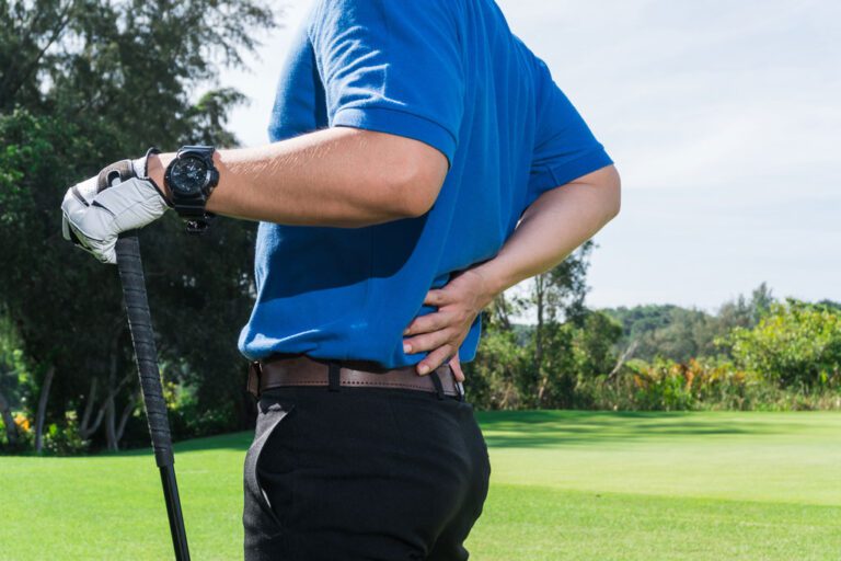 A golfer in a blue shirt holds his back which is in pain