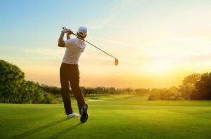 A golfer tee's off sucessfully on the 1st hole of a bright new morning with the sun rising in the horizon